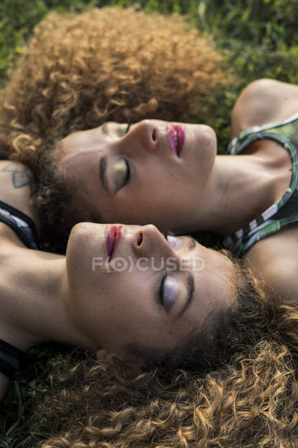 Portrait of rouged twin sisters lying side by side on a meadow — Stock Photo