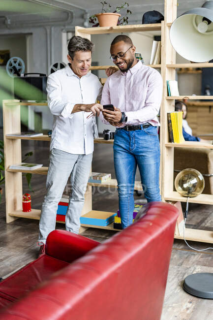 Zwei lächelnde Geschäftsleute mit Handy im Loft-Büro — Stockfoto