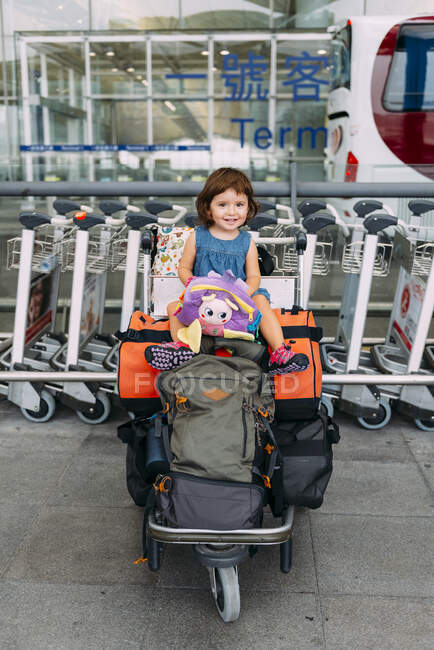 Niña sentada en la parte superior del equipaje en un carro en el aeropuerto — Stock Photo