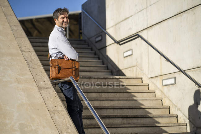 Mature man with a shoulder bag standing on stairs in the city — Stock Photo