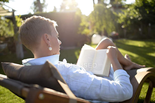 Donna sulla sedia a sdraio lettura libro in giardino — Foto stock