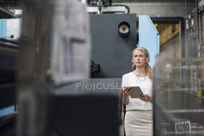 Женщина с планшетом на станке в цехе завода смотрит вокруг — стоковое фото