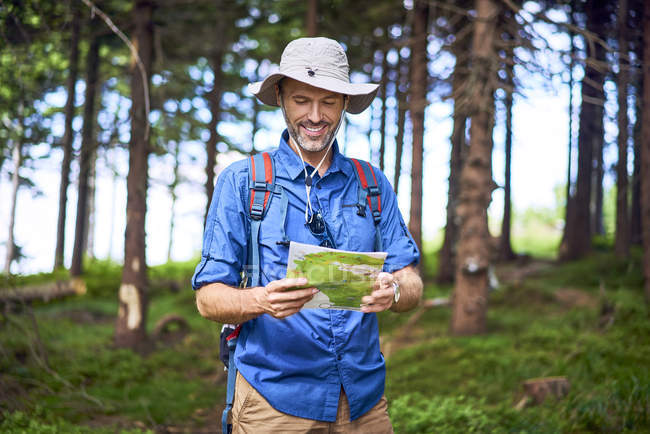 Hombre sonriente mirando el mapa durante una caminata en el bosque - foto de stock