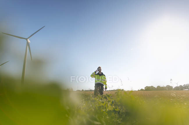 Инженер, стоящий в поле на ветряной электростанции и разговаривающий по мобильному телефону — стоковое фото