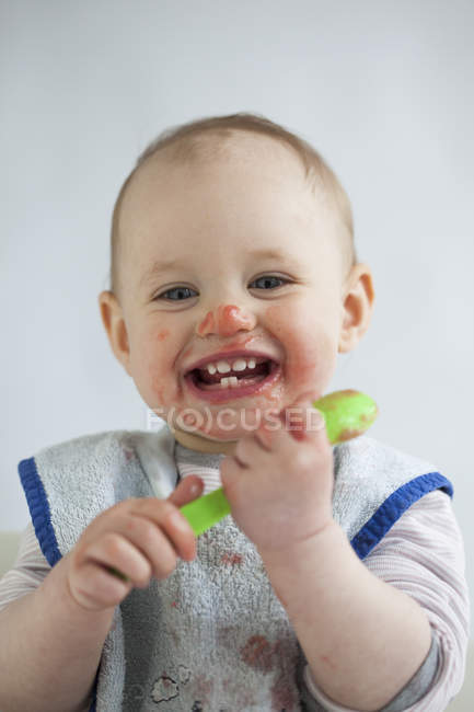 Portrait of laughing baby girl eating mush — Stock Photo