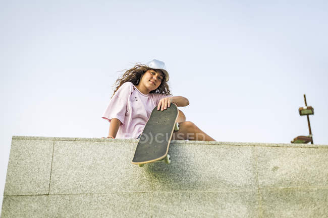Девушка со скейтбордом сидит на стене — стоковое фото