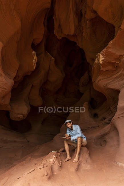 Jeune homme assis dans une grotte, prenant des notes — Photo de stock