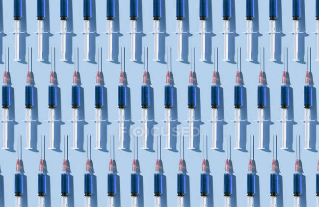 Múltiples jeringuillas organizadas en un patrón sobre fondo azul - foto de stock
