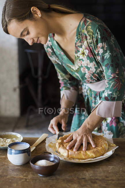 Jeune femme coupant gâteau fait maison — Photo de stock