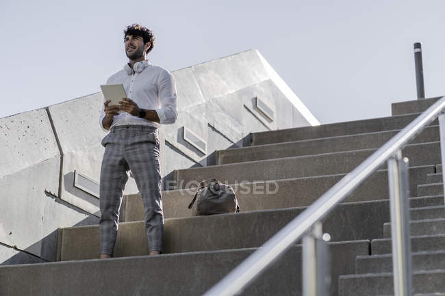 Jeune homme debout sur les escaliers à l'extérieur et tenant la tablette — Photo de stock