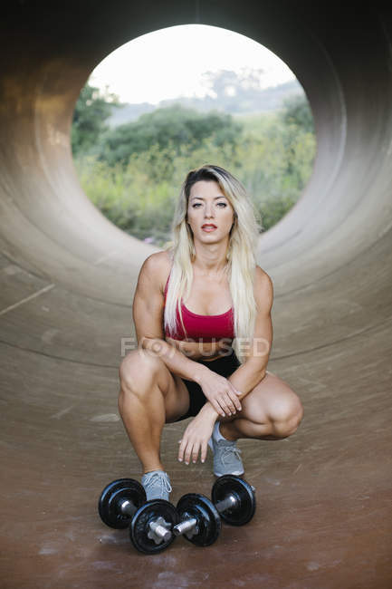 Athletic woman crouching inside a tube with dumbbells — Stock Photo