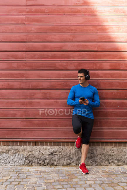 Sportler lehnt an Hauswand und hält Handy in der Hand — Stockfoto