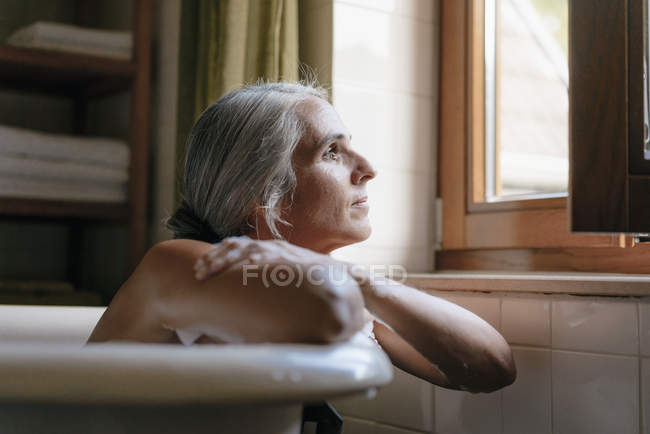 Portrait of pensive woman in bathtub looking out of window — Stock Photo