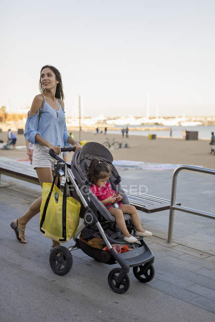 Mutter spaziert mit ihrer Tochter im Kinderwagen an der Strandpromenade — Stockfoto