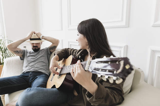 Розслаблена пара сидить на дивані, жінка грає на гітарі вдома. — стокове фото