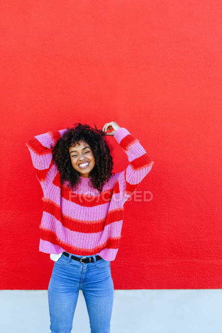 Portrait of laughing young woman with curly hair standing in front of red wall — Stock Photo