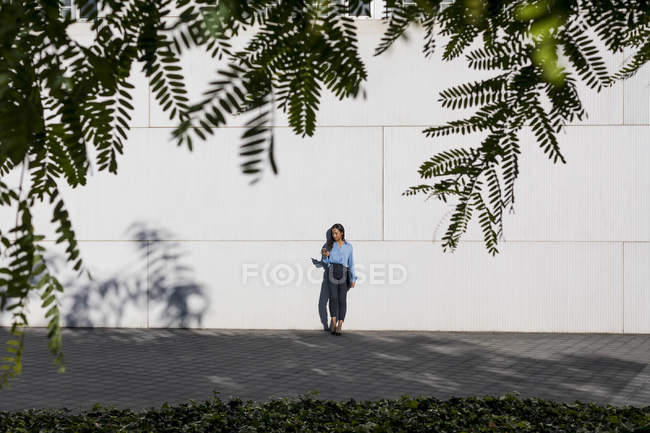 Empresária usando smartphone, segurando saco de laptop — Fotografia de Stock