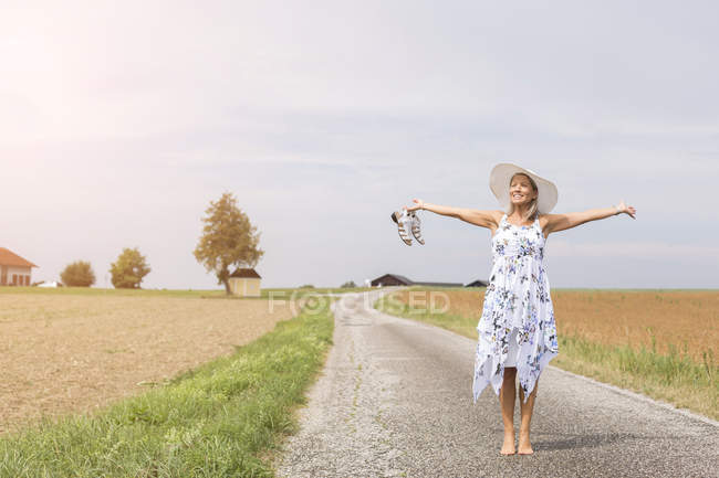 Mature woman standing on remote country lane in summer with outstretched arms — Stock Photo