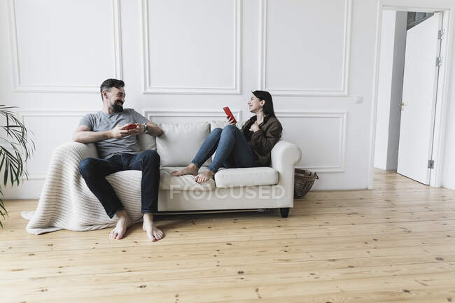 Пара сидить вдома на дивані, користуючись смартфонами. — стокове фото