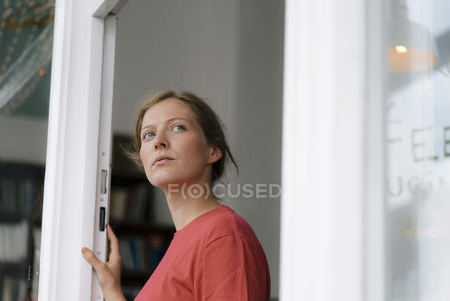 Молодая женщина у французской двери в кафе оглядывается вокруг — стоковое фото