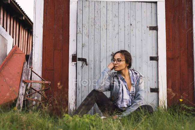 Portrait d'une jeune femme assise dans l'herbe devant une cabane en bois — Photo de stock