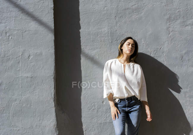 Portrait of young woman leaning against grey wall — Stock Photo