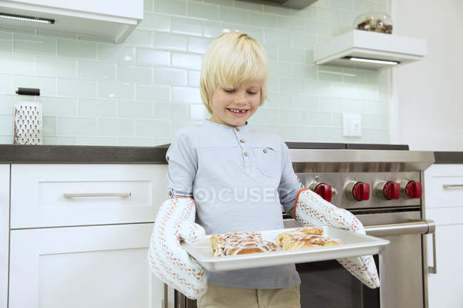 Smiling boy holding baking tray with cinammon buns — Stock Photo