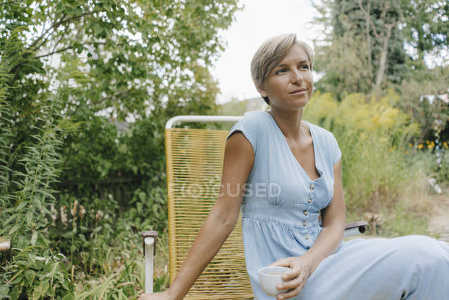 Frau sitzt mit Tasse Kaffee im Garten — Stockfoto