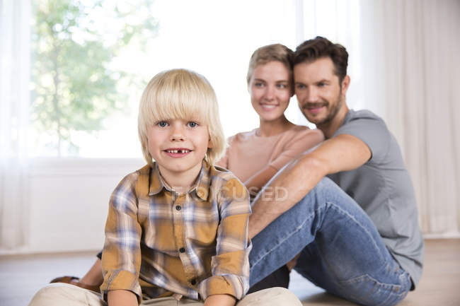 Retrato de menino sorridente com os pais no fundo sentado no chão em casa — Fotografia de Stock