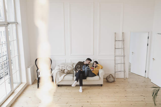 Coppia seduta sul divano nel soggiorno di nuova casa guardando il cellulare — Foto stock