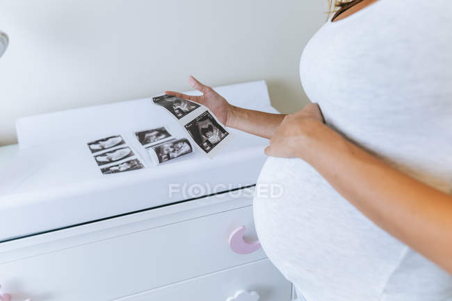 Primer plano de la mujer embarazada mirando imágenes de ultrasonido en la habitación del bebé - foto de stock