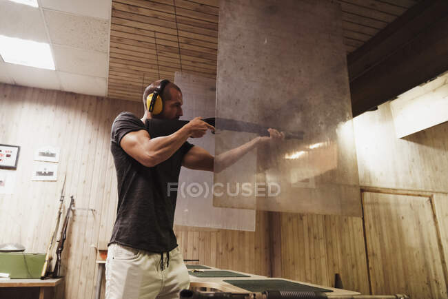 Hombre apuntando con un rifle en un campo de tiro interior - foto de stock
