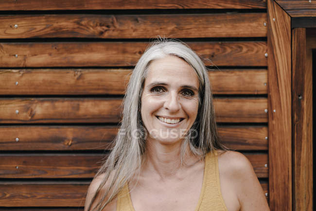 Portrait of smiling mature woman in front of wooden facade — Stock Photo