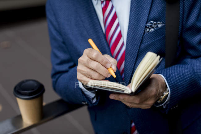 Close-up of businessman writing in diary outdoors — Stock Photo