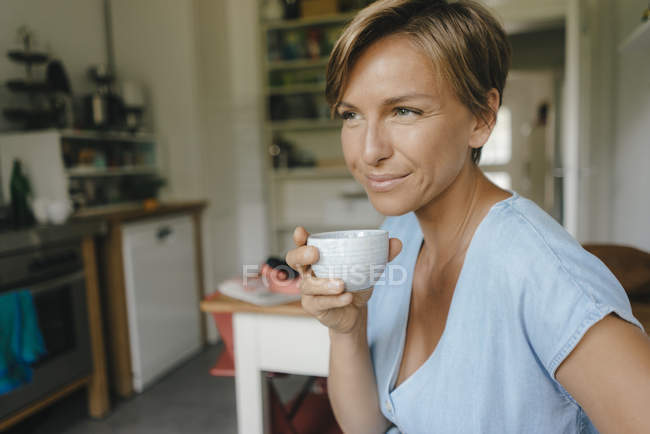 Улыбающаяся женщина дома пьет кофе — стоковое фото