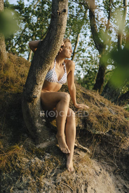 Woman wearing a bikini and sitting at a tree — Stock Photo
