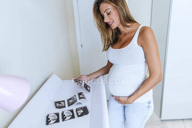 Mujer embarazada mirando imágenes de ultrasonido en la habitación del bebé - foto de stock