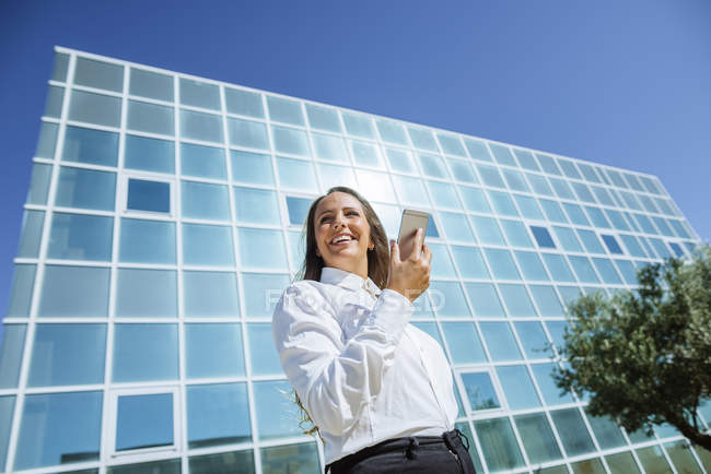 Усміхнена бізнес-леді використовує мобільний телефон за межами офісної будівлі — стокове фото