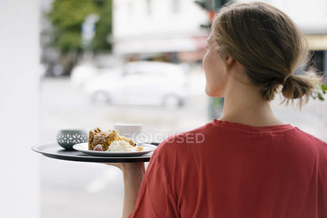 Rückansicht einer jungen Frau, die in einem Café Kaffee und Kuchen serviert — Stockfoto