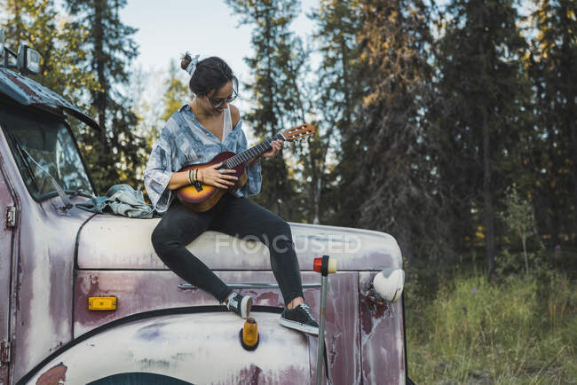 Young woman sitting on a broken truck, playing the ukulele — Stock Photo