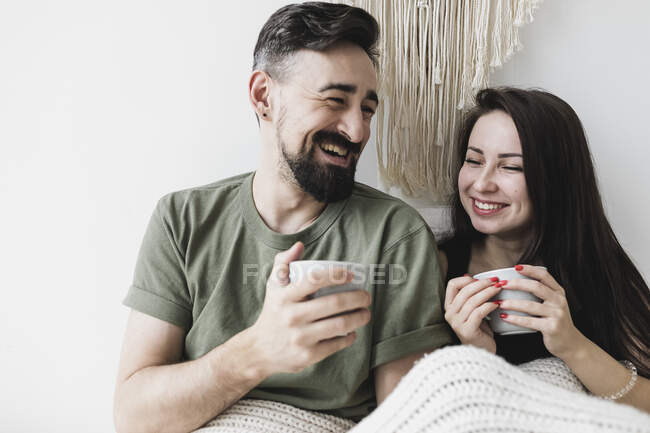 Feliz casal sentado na cama, beber café, se divertindo — Fotografia de Stock