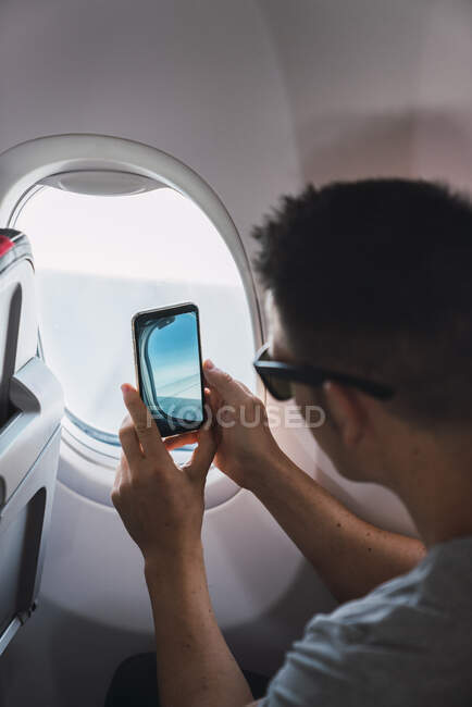 Uomo in aereo, utilizzando smartphone, scattando una foto, finestra dell'aereo — Foto stock