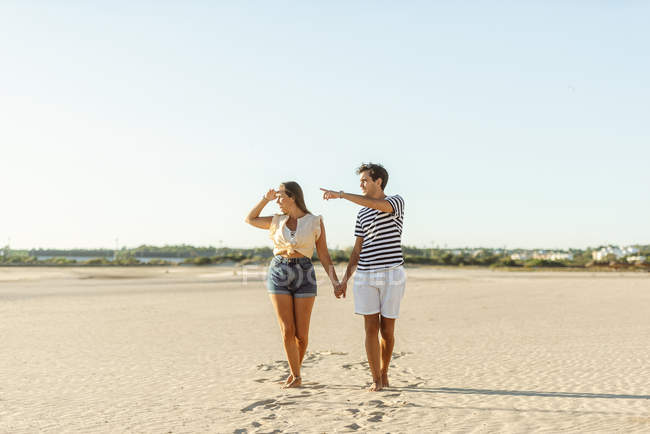 Giovane coppia che cammina mano nella mano sulla spiaggia — Foto stock