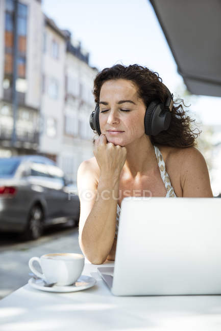 Frau sitzt im Café, trägt Kopfhörer, benutzt Laptop — Stockfoto