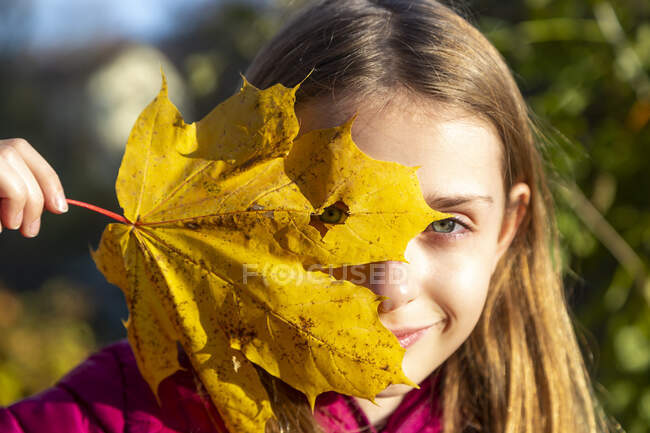 Portrait of smiling girl looking through hole in autumn leaf — Stock Photo