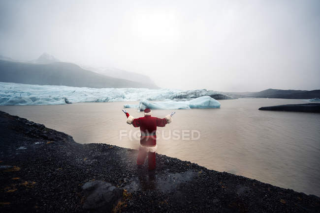 Iceland Rear View Of A Man Disguised As Santa Claus Standing At A Glacier Raising His Arms Lake Power Stock Photo