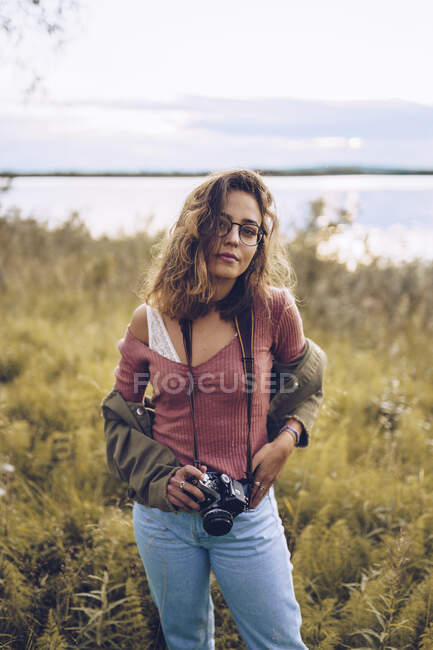 Junge Frau mit Kamera steht am Seeufer — Stockfoto
