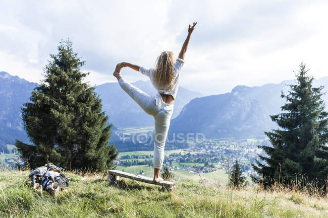 Germania, Baviera, Oberammergau, giovane donna che fa yoga sulla panchina sul prato di montagna — Foto stock