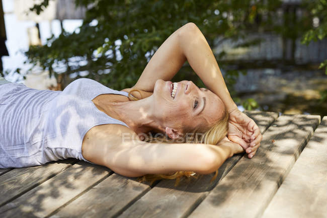 Happy blond woman lying on wooden jetty at a lake — Stock Photo