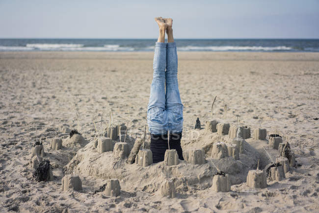 Mujer madura haciendo una cabecera en la playa en un castillo de arena - foto de stock